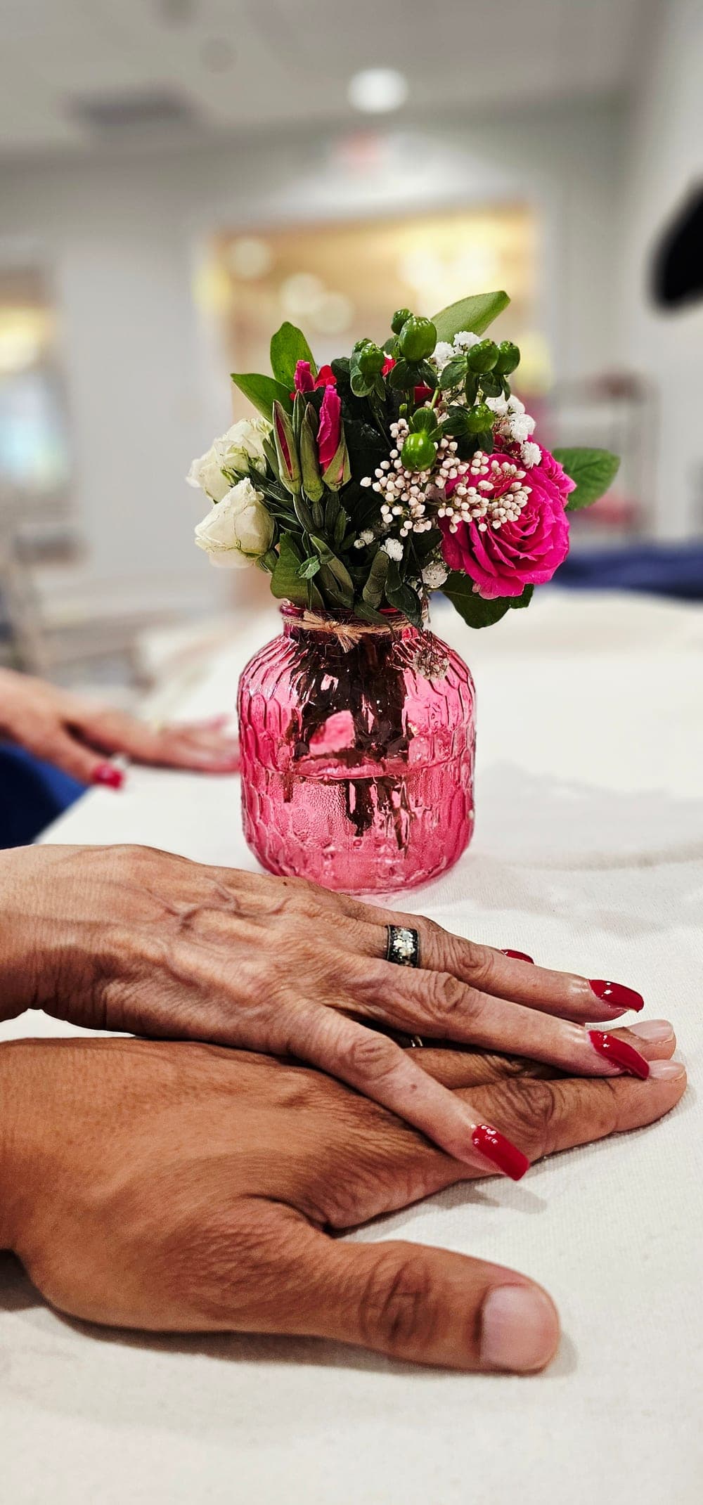 Corey and his mother's hands resting together beside a small vase of flowers