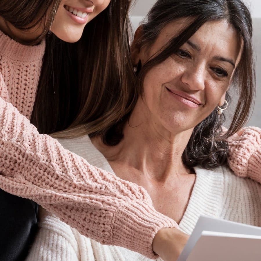 A woman hugging her mother from behind, both smiling