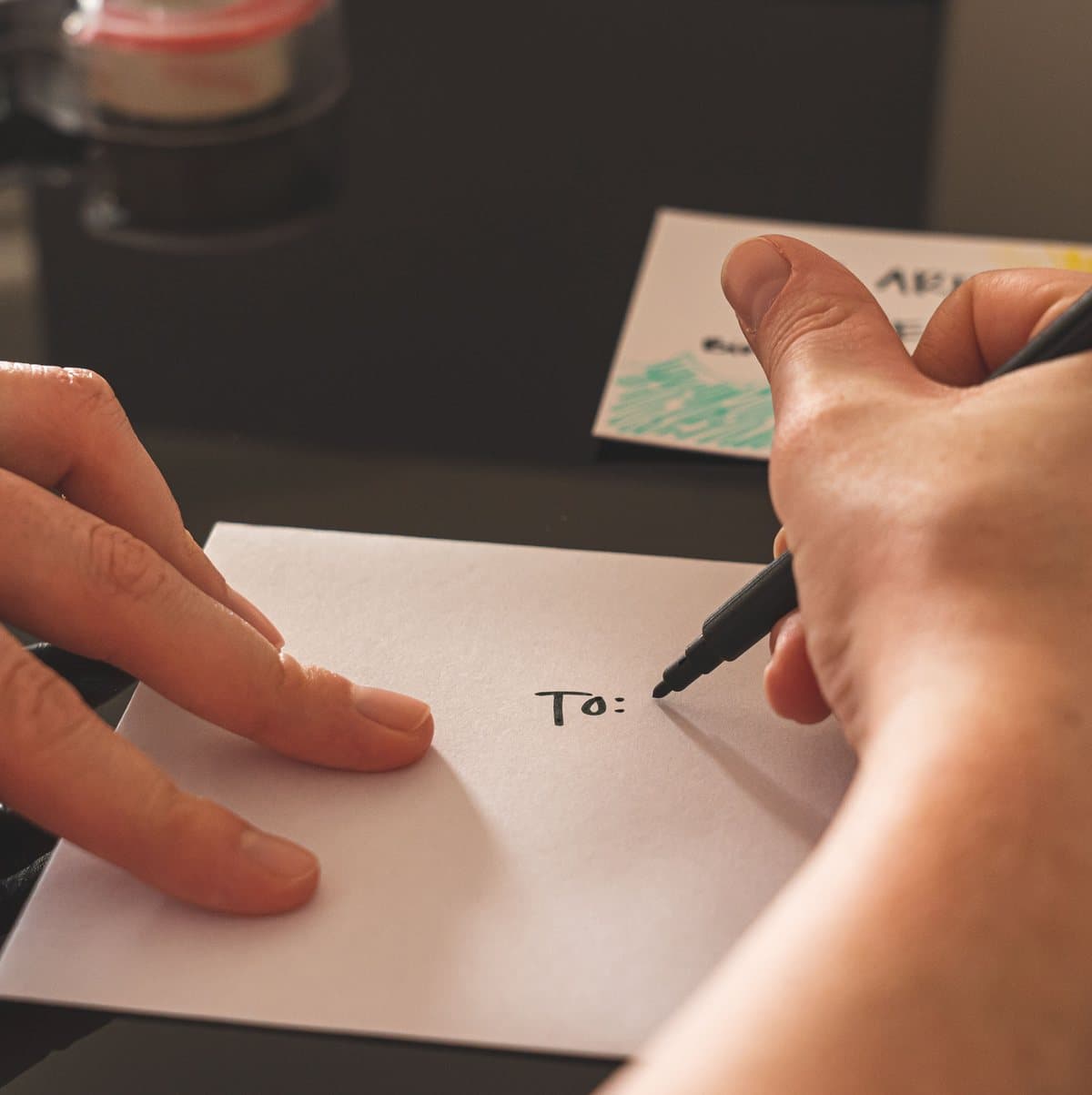 A hand addressing a card, writing "To:" with a marker