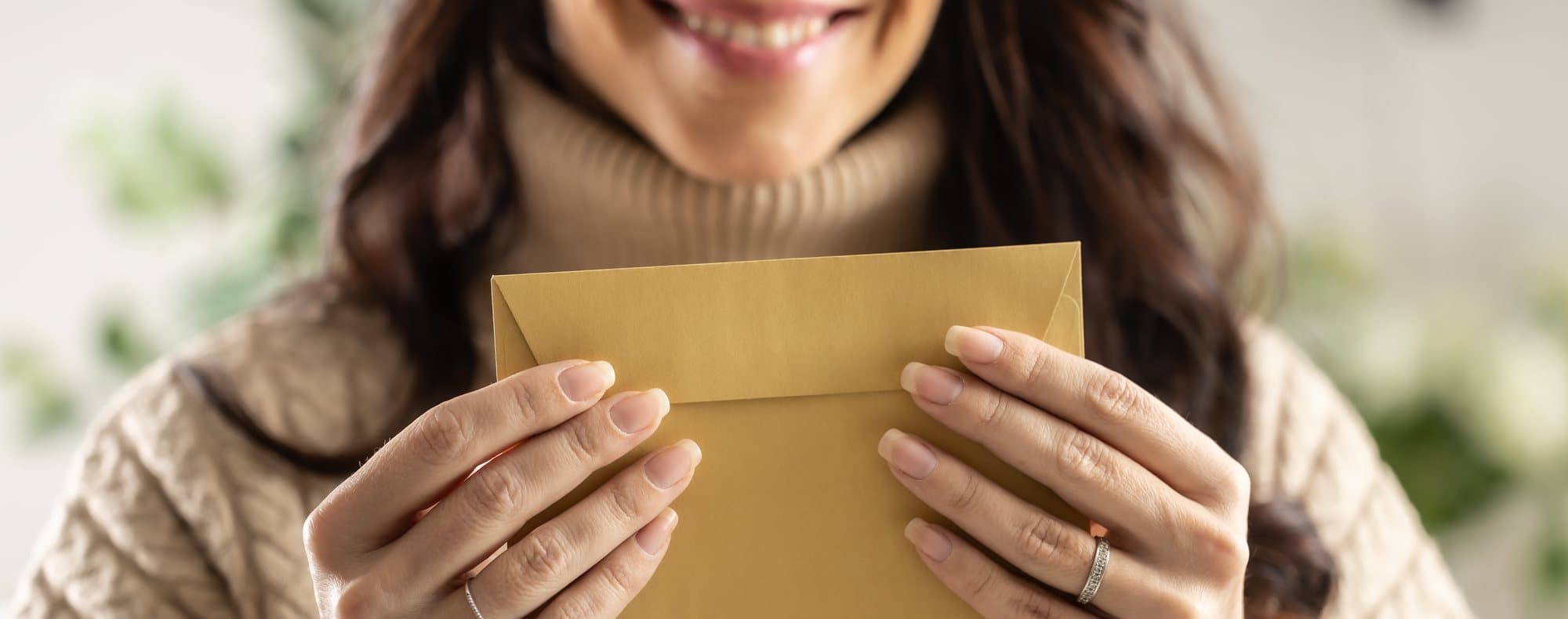 A woman smiling as she opens a kraft envelope