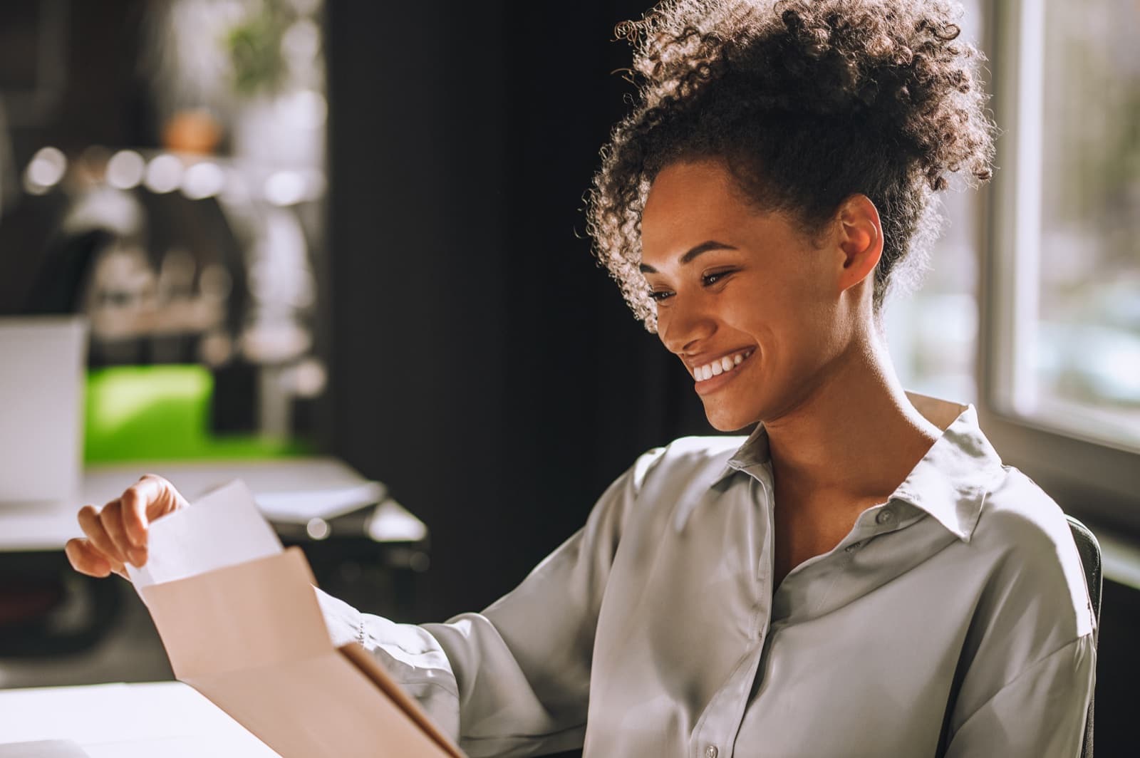 A woman smiling as she reads a card at her desk
