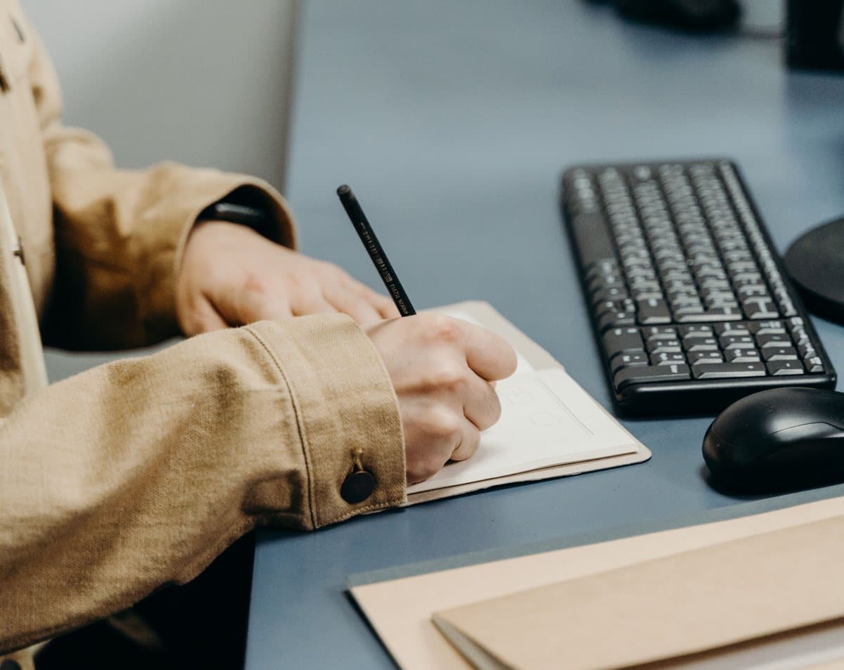 Someone writing a note at a desk beside a keyboard